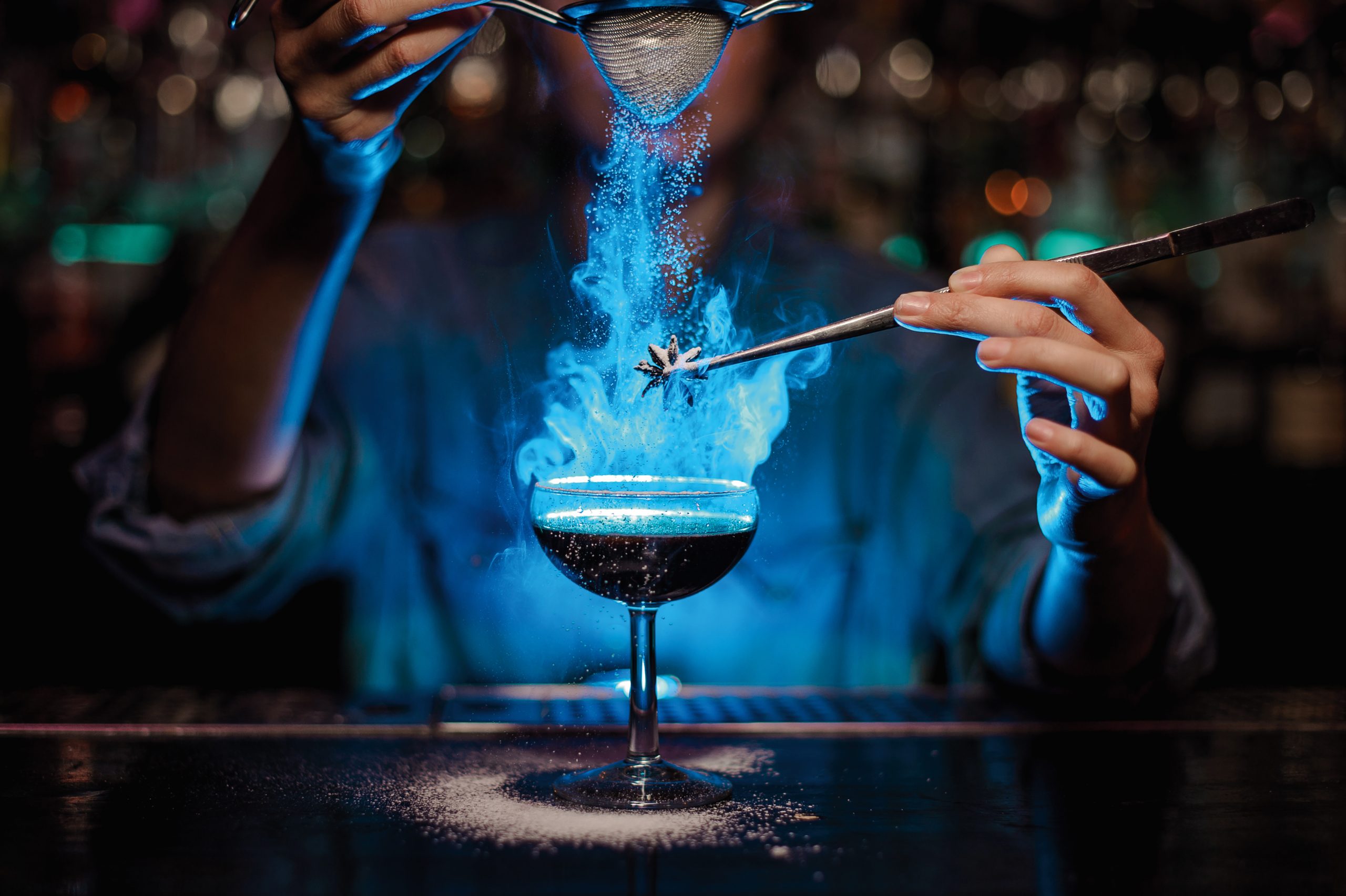 Ein Barkeeper kreiert einen Cocktail, wobei blau leuchtender Rauch und andere visuelle Effekte verwendet werden, um das Getränk beeindruckend zu präsentieren.